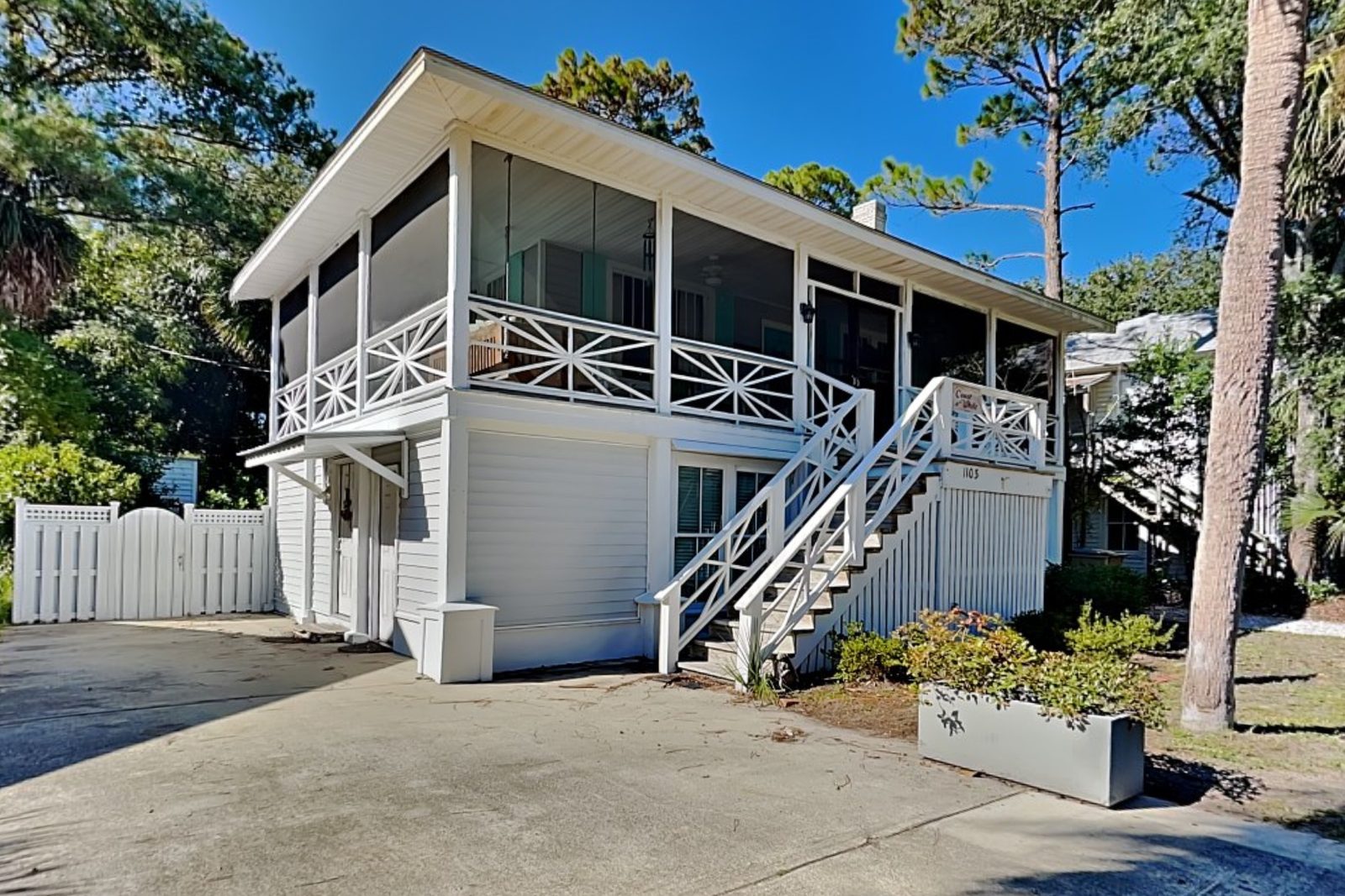 1103 2nd Avenue: a raised white beach cottage with a screened porch and a wide concrete driveway