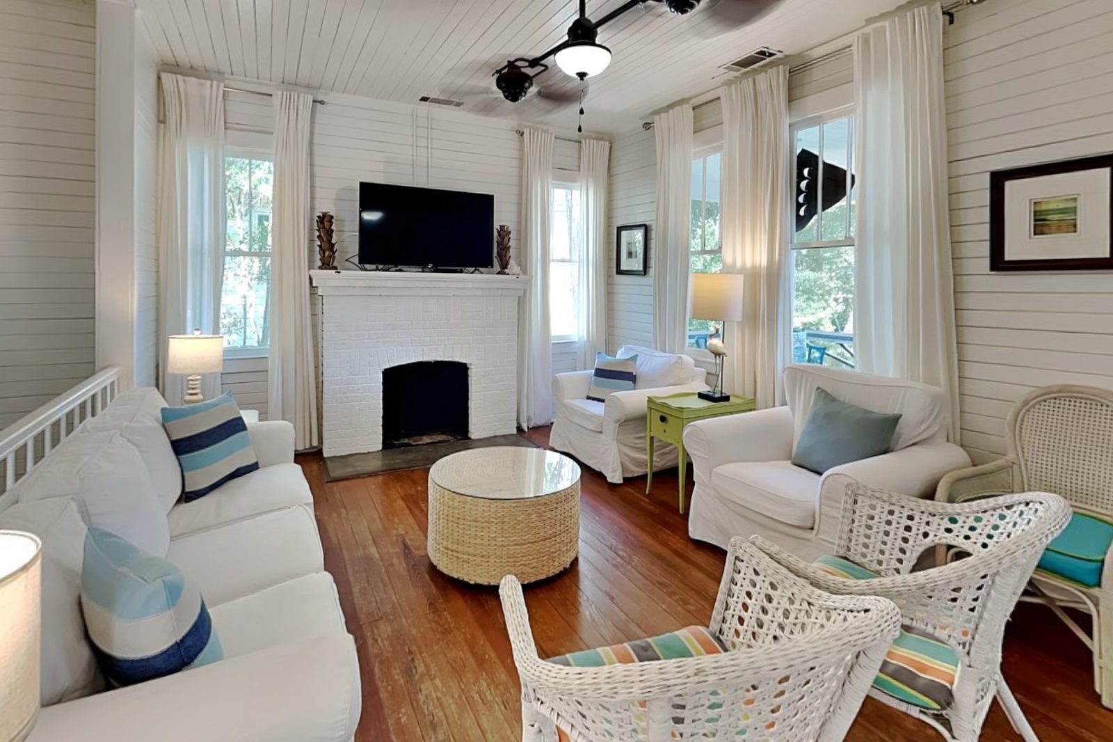 Living room with shiplap walls, a white brick fireplace, heart pine floors and wicker chairs