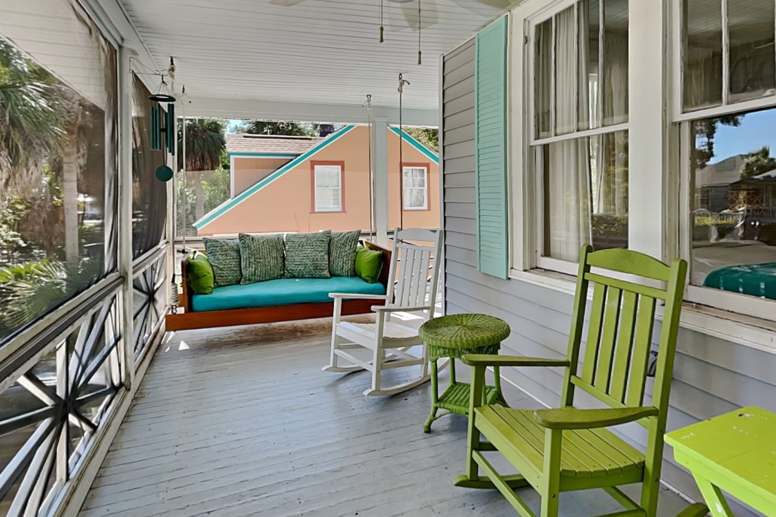Screened porch with a hanging swing bed and green rocking chairs